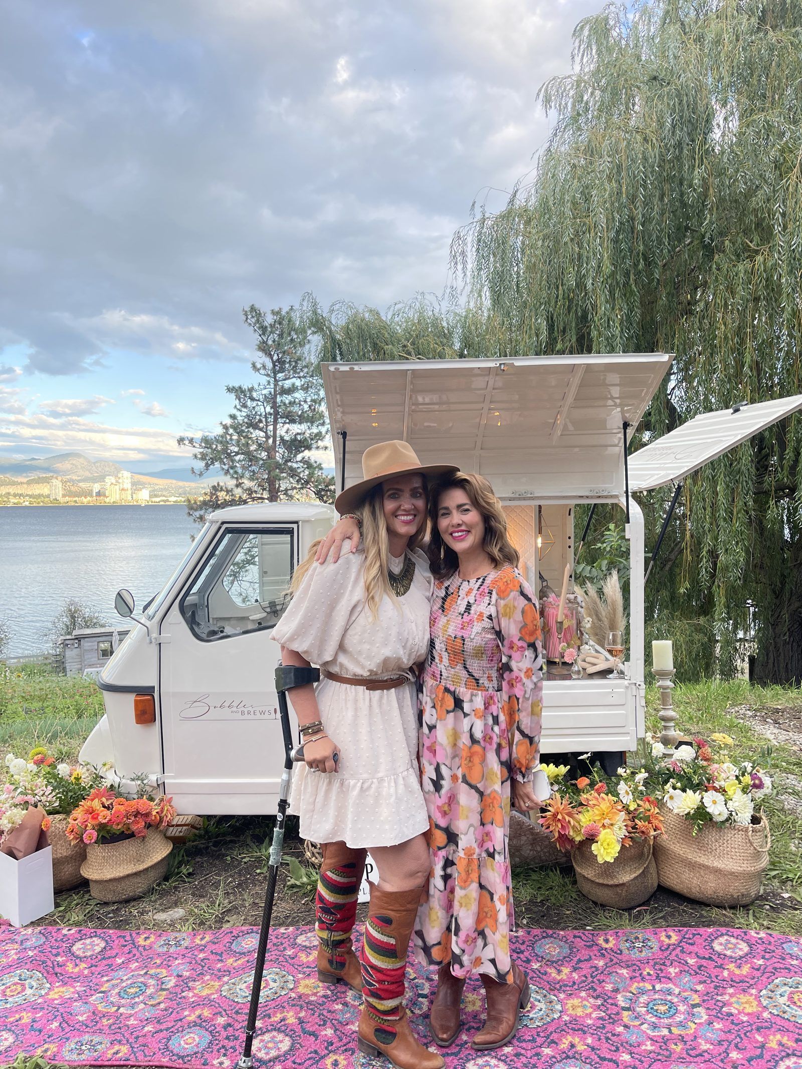 Friends celebrating lakeside in front of the Bubbles and Brews prosecco bar with a willow tree and city skyline in the background