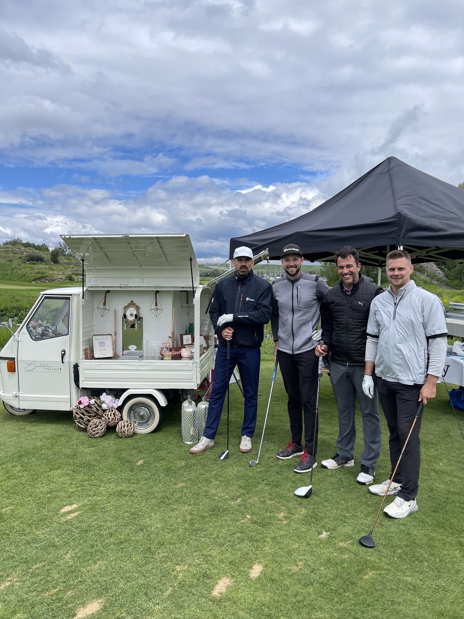 Group of golfers gathered around the Bubbles and Brews mobile bar at an Alberta golf tournament