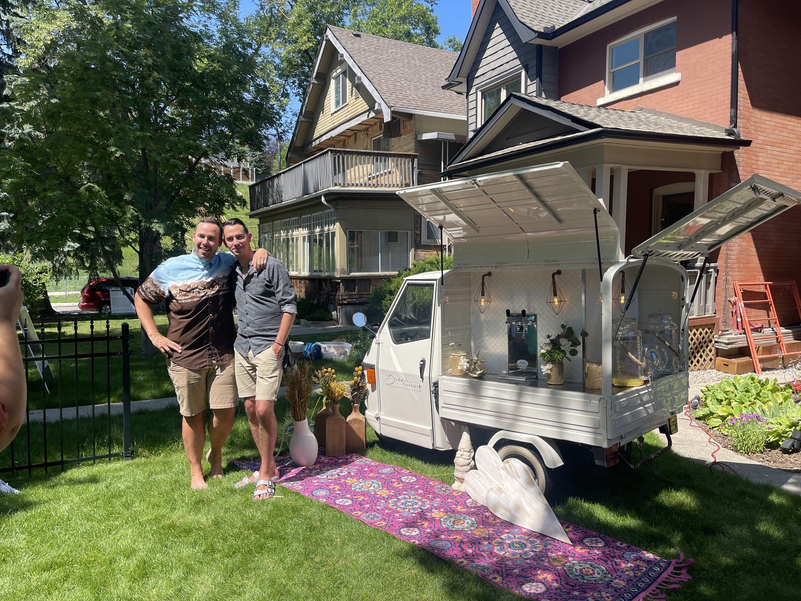 Two guests celebrating together at a Stampede-season backyard party in Calgary, in front of the open Bubbles and Brews mobile bar