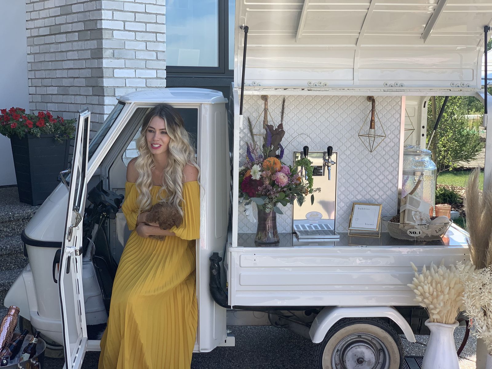 Guest in a yellow dress holding a small dog at the open Bubbles and Brews mobile bar
