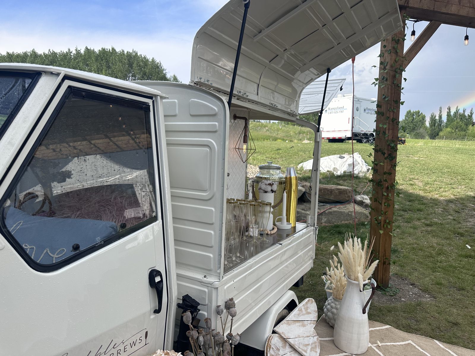 Vintage Piaggio Ape mobile bar set up under a pergola at a mountain-view Alberta venue