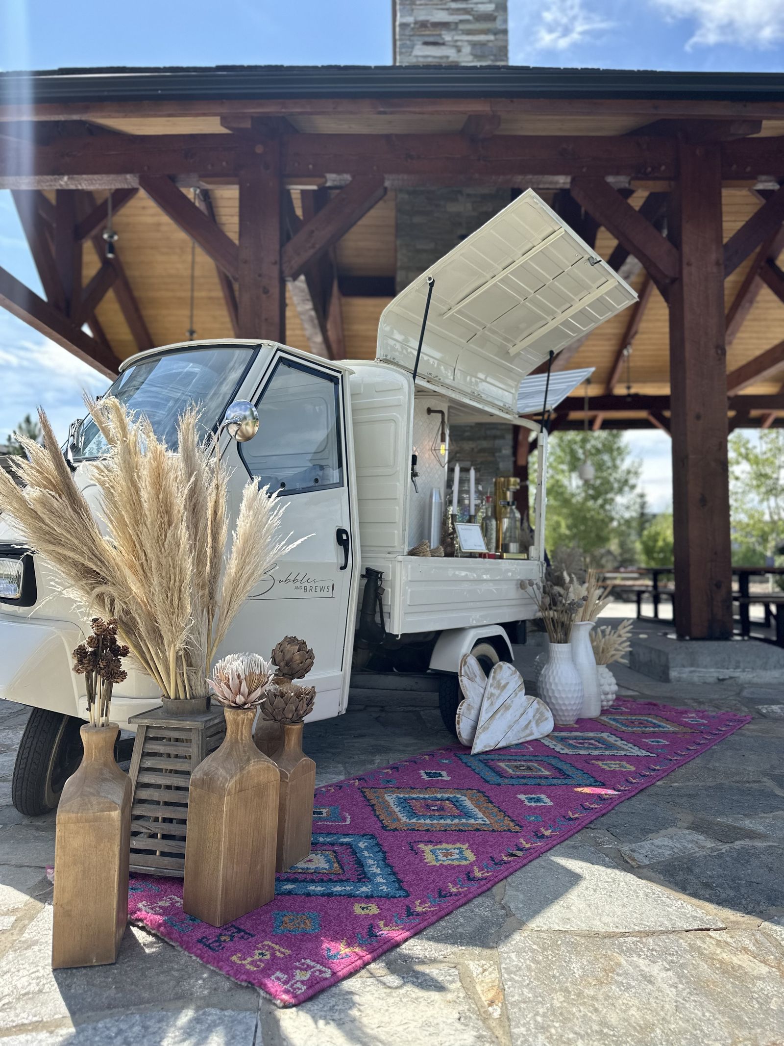 Boho-styled mobile bar under a timber pavilion with a Persian kilim rug at an Alberta wedding venue