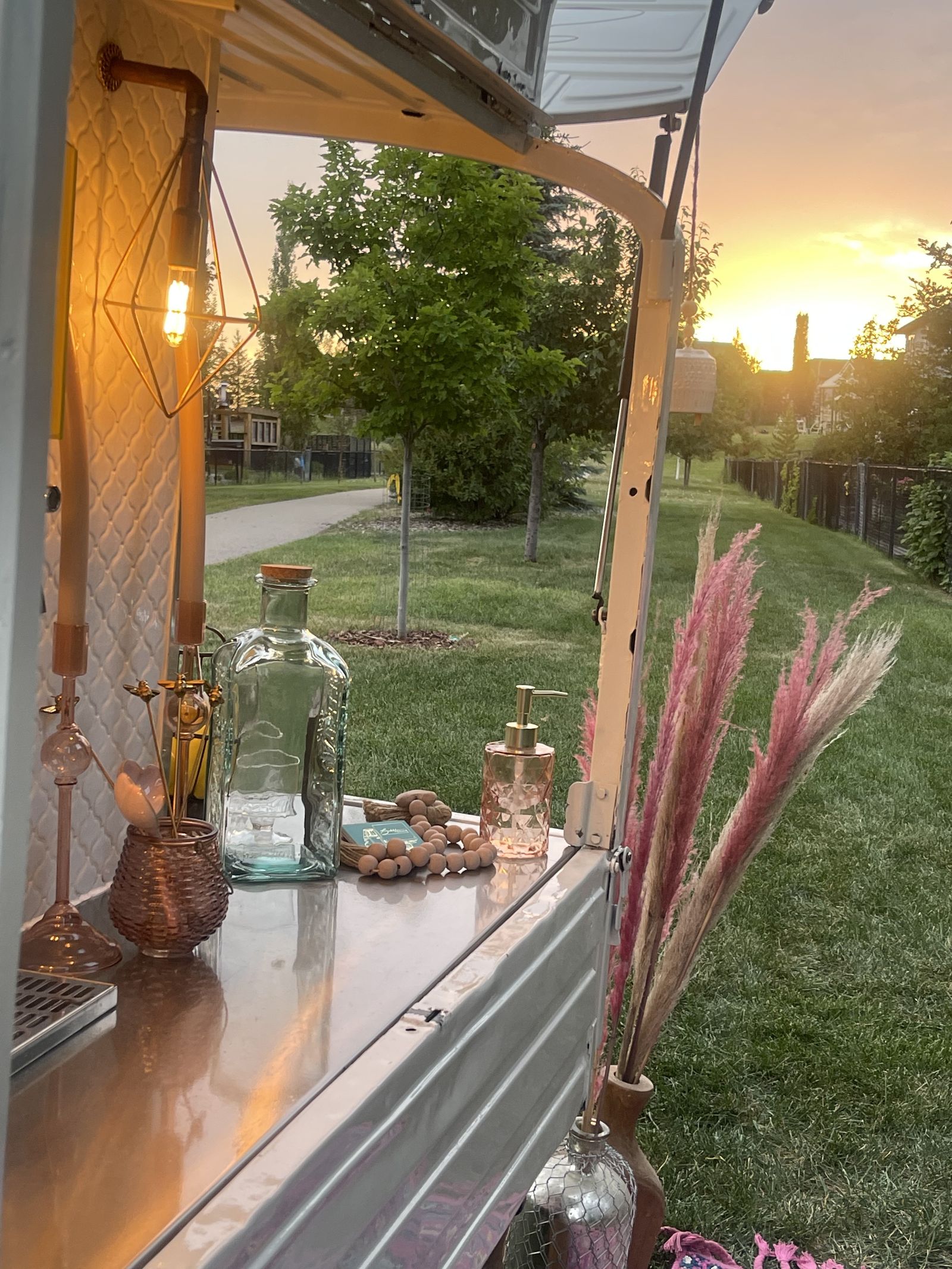 Golden hour sunset view from inside the Calgary mobile bar overlooking a residential green space