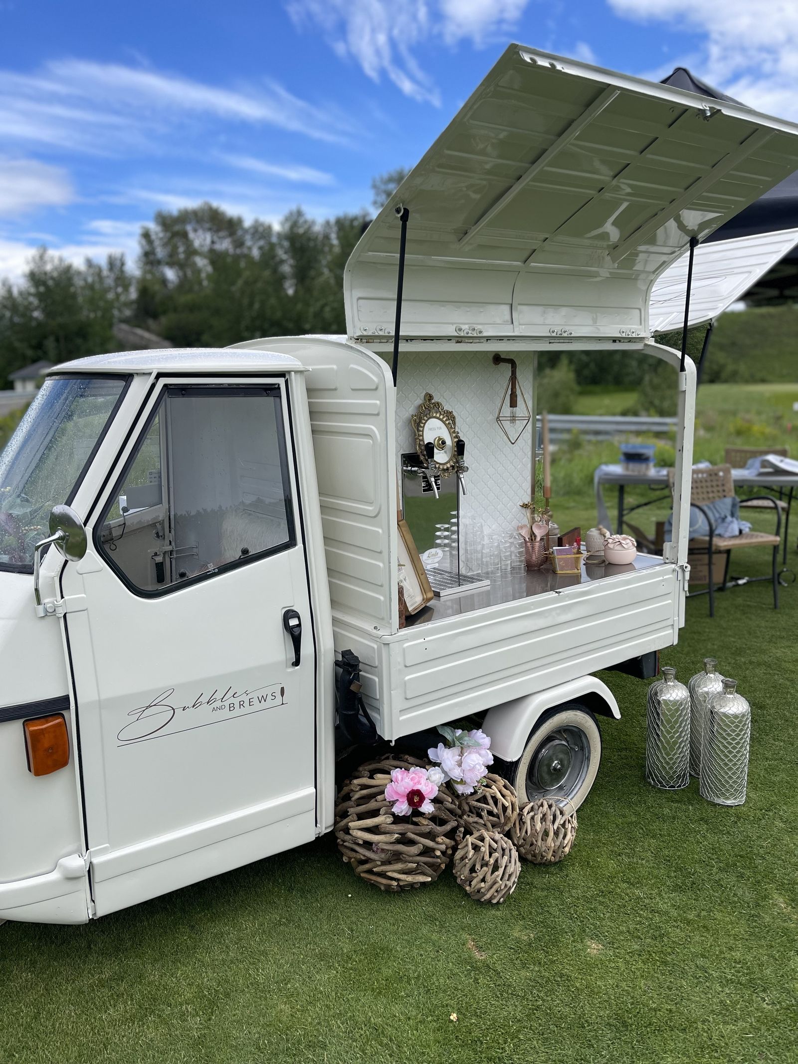 Full Piaggio Ape mobile bar with fresh peonies and decorative styling on a sunny day in Calgary