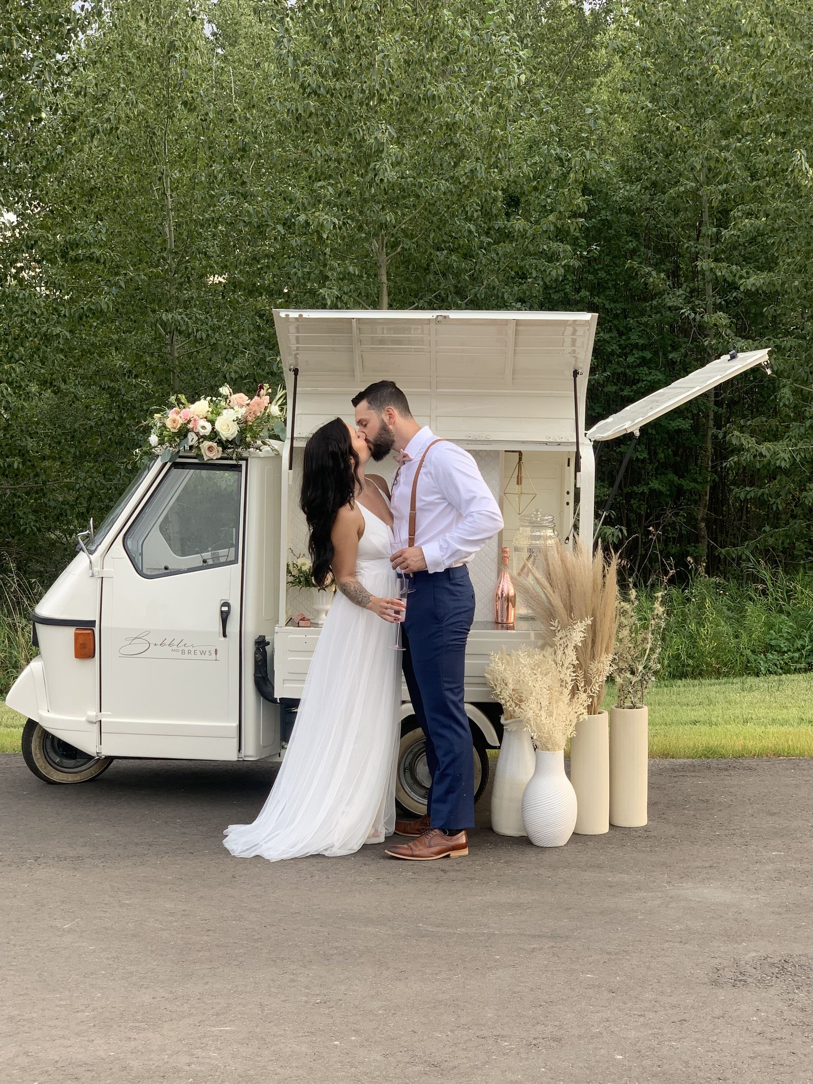 Bride and groom sharing a kiss in front of the open Piaggio Ape mobile bar