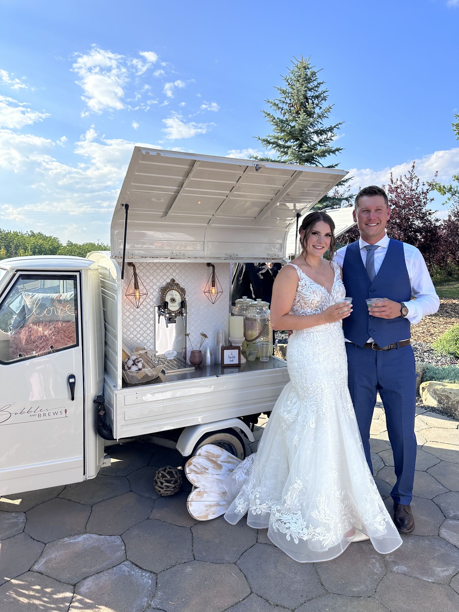 Bride and groom posed beside the Bubbles and Brews mobile bar at a mountain resort wedding near Banff